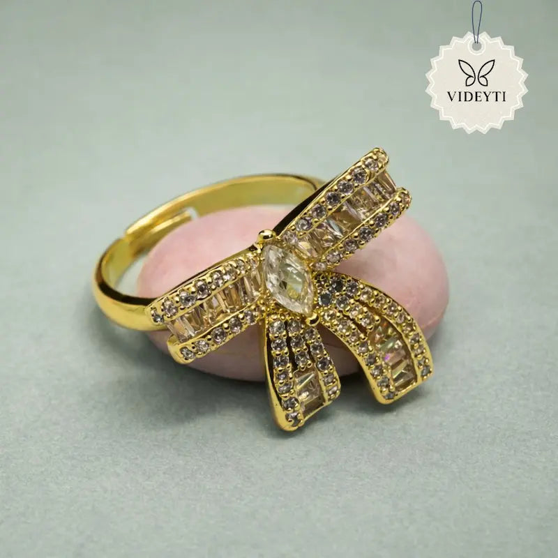 Gold stainless steel ring with rhinestone-studded bow and central crystal; adjustable anti-tarnish Korean style design.