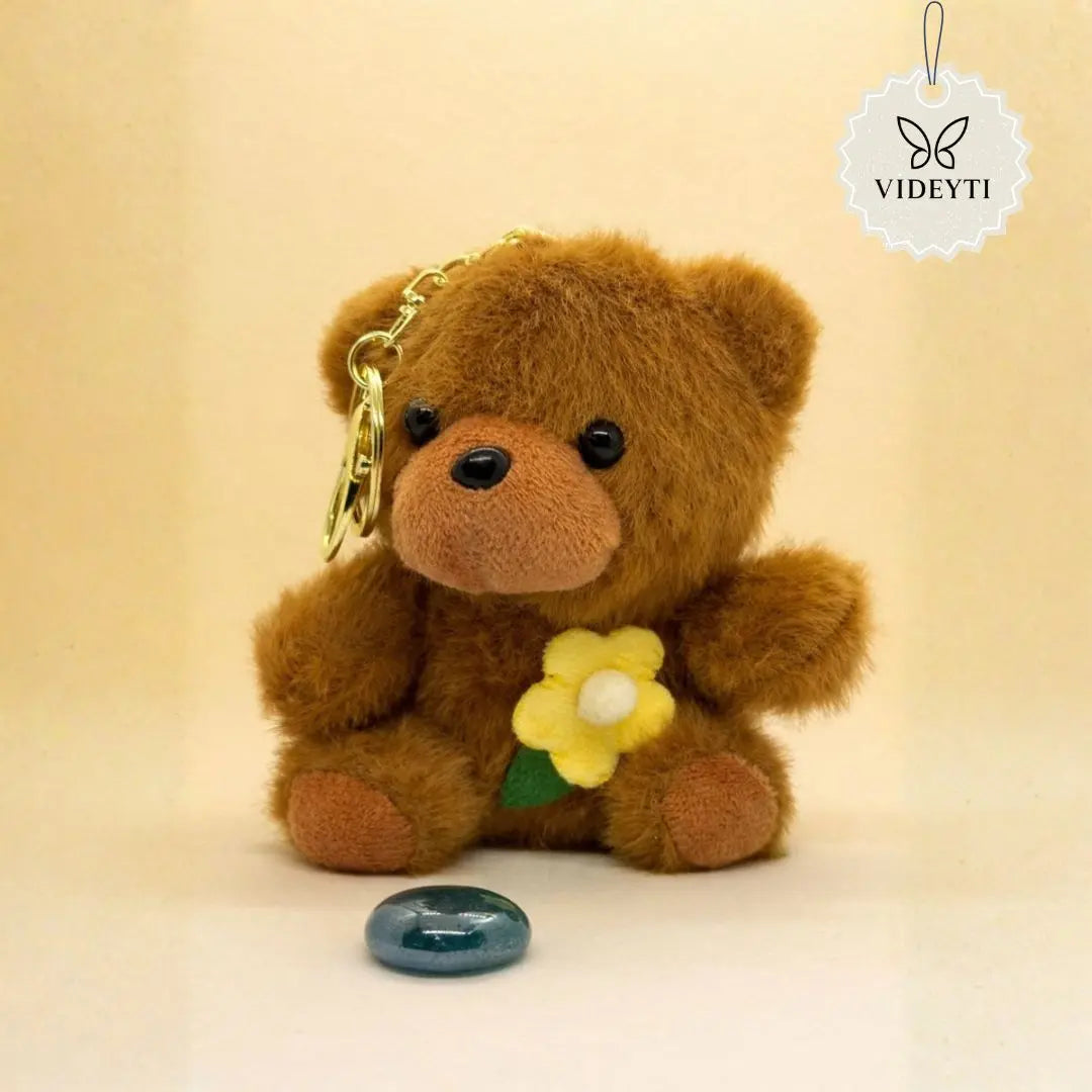 Brown plush teddy bear bag charm with yellow flower accent and gold keychain ring.