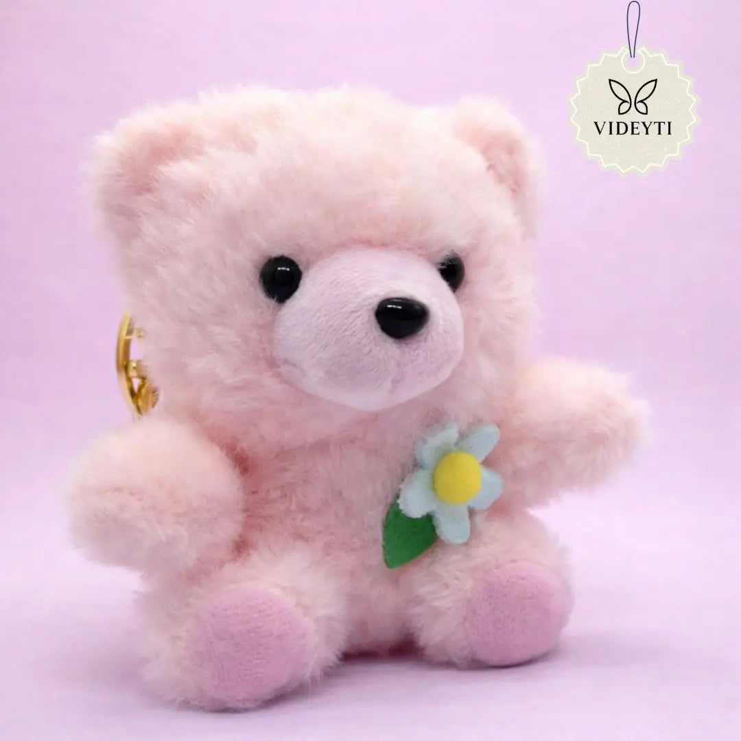 Pink plush teddy bear bag charm with pink flower accent and gold keychain ring.